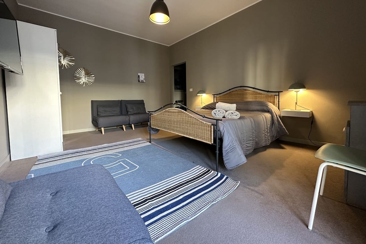 A modern bedroom with a bed, bedside tables, a desk, a sofa, and a hanging light fixture.