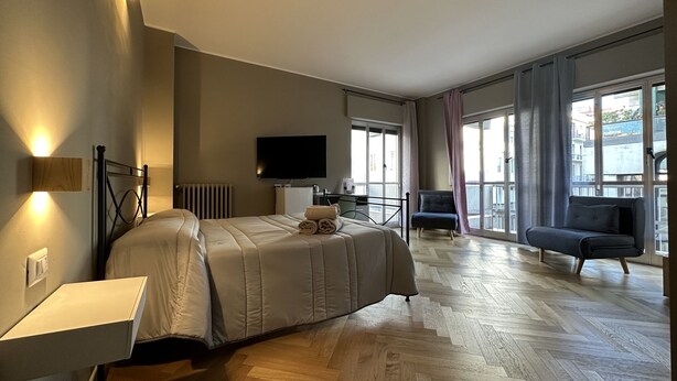 Ein modernes Hotelzimmer mit einem großen Bett, einem Flachbildfernseher, einer Couch und Blick auf die Stadt durch große Fenster.