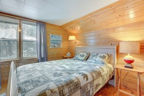 Ett mysigt sovrum med ett träpanelat tak, en stor säng med ett täcke, två sänglampor och ett fönster med gardiner.