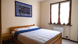 A bedroom with a wooden bed, a nightstand, a window with curtains, and a wall hanging. - Inviting 1-bed Apartment With Box and Seeviews (Ranzanico)