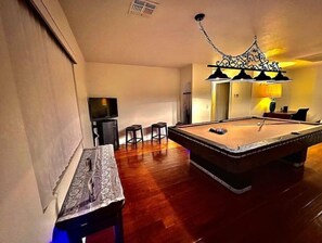 Enjoy a game of pool or unwind with a drink at the bar area, featuring a TV and comfortable seating.