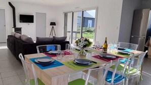 Una sala de estar moderna con un sofá, una mesa de comedor para cuatro personas, un televisor y una zona de cocina con un refrigerador.