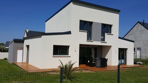 Una casa moderna de dos pisos con techo plano, ventanas amplias y un patio cubierto.