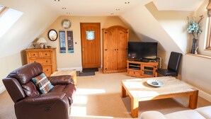 A cozy living room with a leather sofa, a wooden cabinet, a television, and a coffee table. - Granary Loft (Grantham)