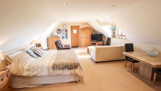 A spacious attic bedroom with a large bed, a sofa, a TV, and a dining area. - Granary Loft (Grantham)