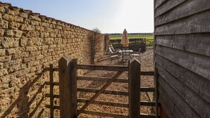 A stone wall with a wooden gate leading to a patio area with a table and chairs, and a view of a field in the distance. - Granary Loft (Grantham)