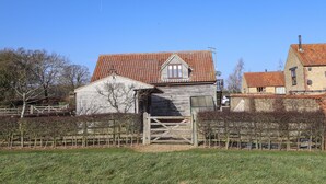 A rustic wooden building with a tiled roof, a small attached shed, and a metal gate. - Granary Loft (Grantham)