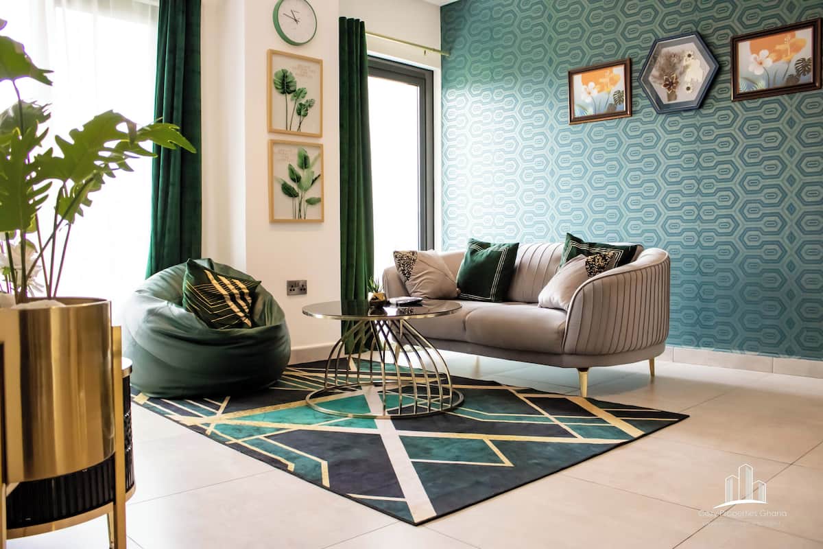 Una sala de estar moderna con un sofá, un sillón de peluche verde, una mesa de centro redonda y una alfombra estampada.