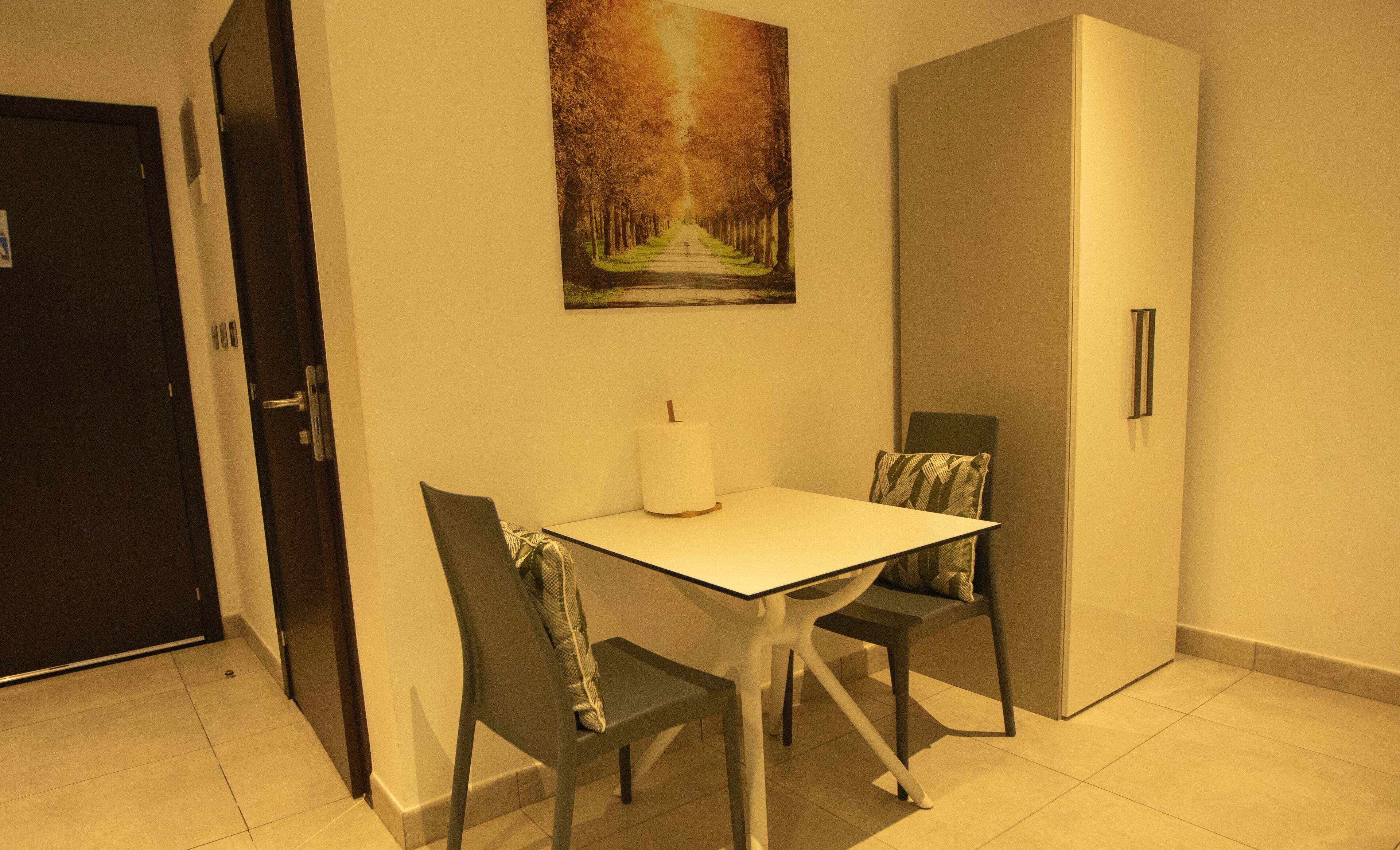 A small dining area with a table and two chairs, a painting on the wall, and a door.