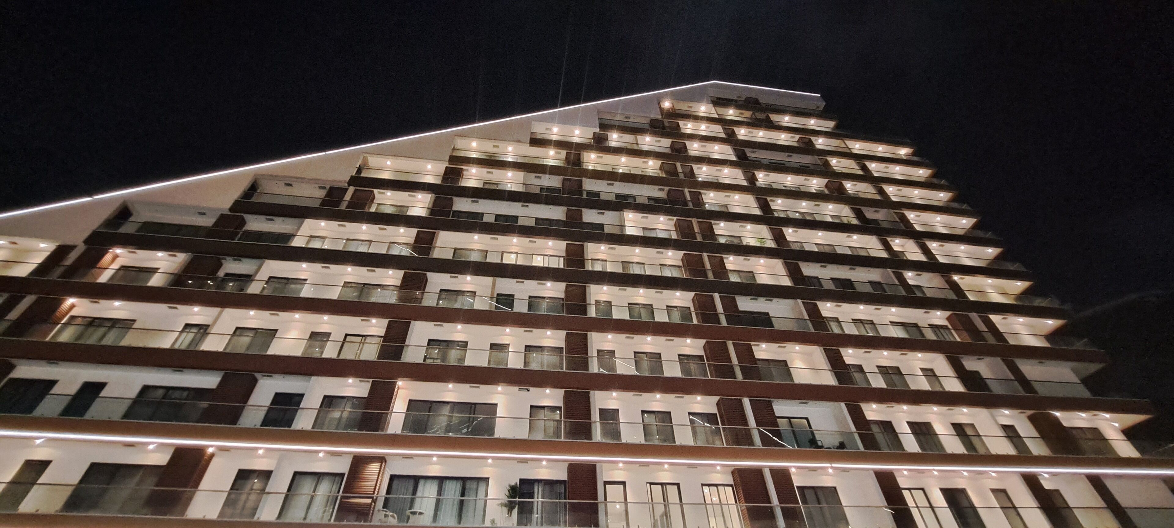A multi-story hotel with a modern design, featuring balconies and a prominent light strip along the top.