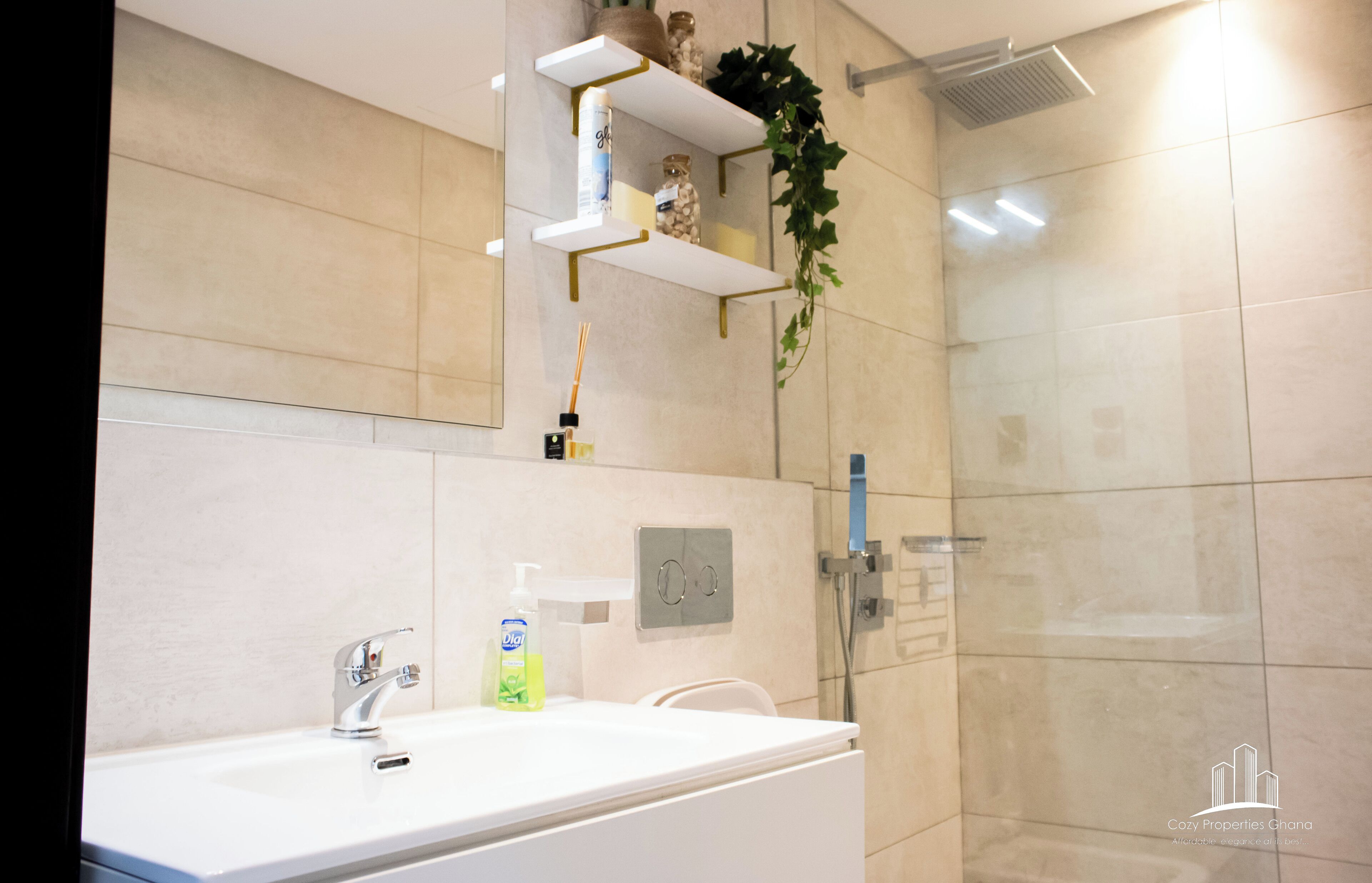 A modern bathroom with a white sink, a mirror, a shower, and a shelf with toiletries.