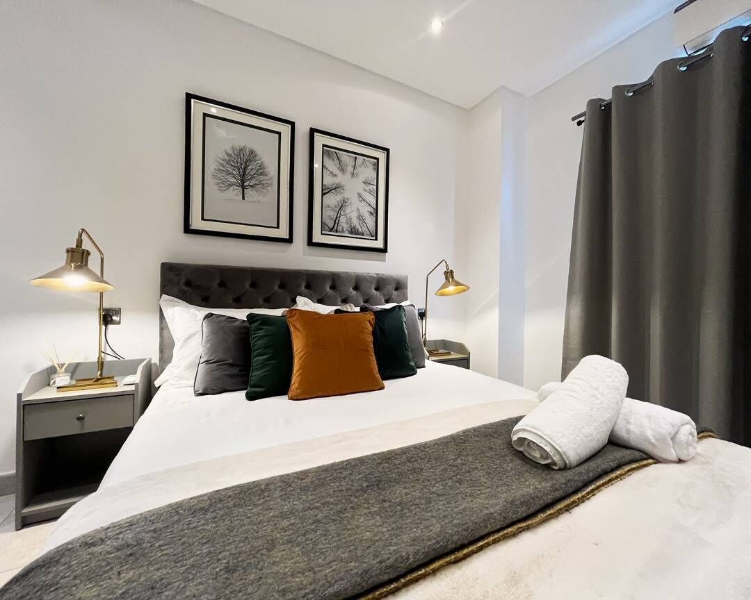 A neatly made bed with a grey throw, two bedside lamps, and two framed pictures on the wall.