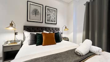 A neatly made bed with a grey throw, two bedside lamps, and two framed pictures on the wall.