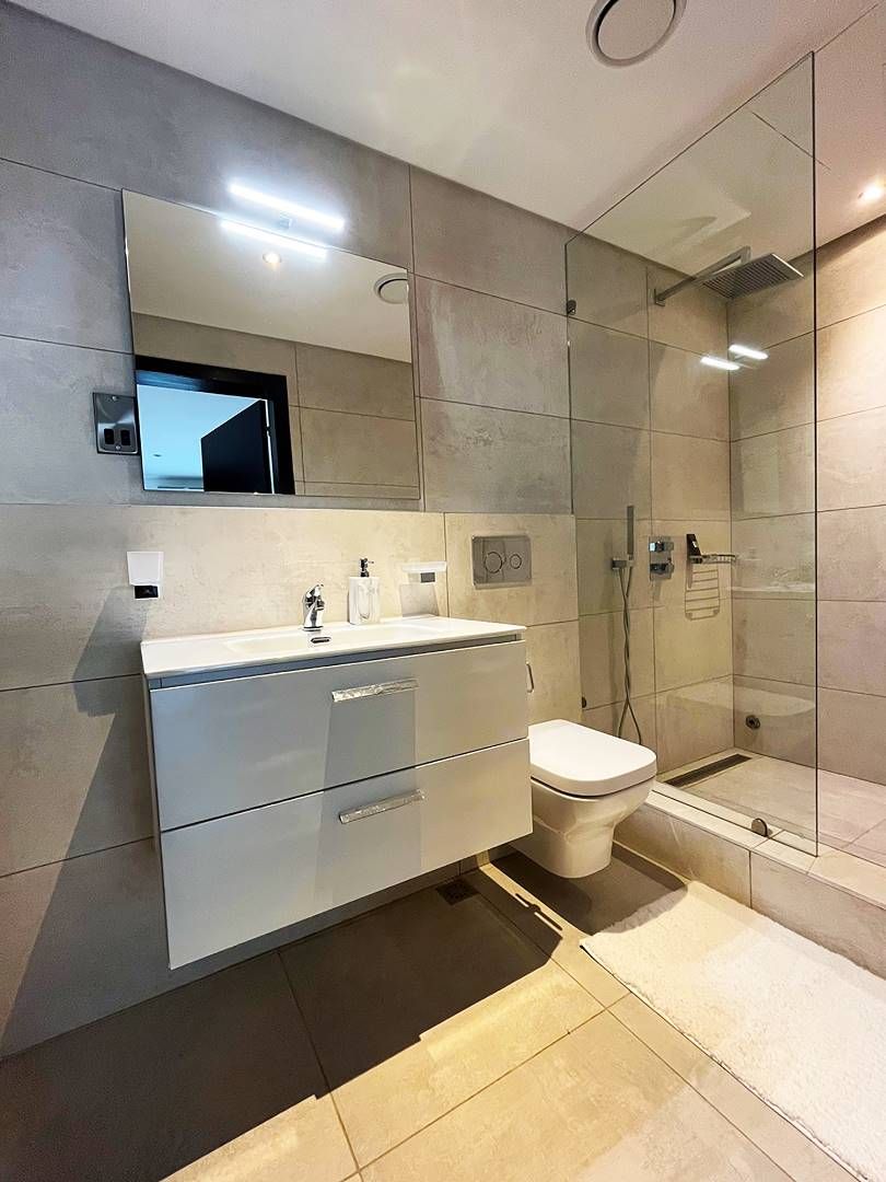 Un baño moderno con cabina de ducha de vidrio, un lavabo blanco con espejo superior y un inodoro.