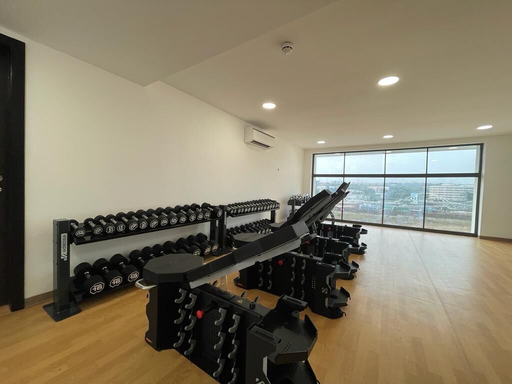 A gym with weightlifting equipment, dumbbells, and a large window offering a city view.