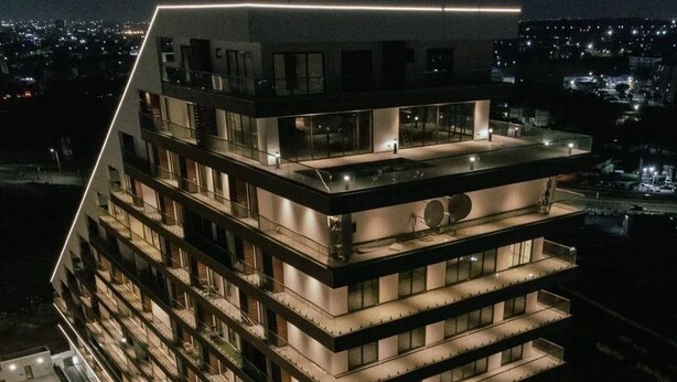 Un hôtel à plusieurs étages au design moderne, doté de balcons à chaque niveau et d’une terrasse sur le toit.