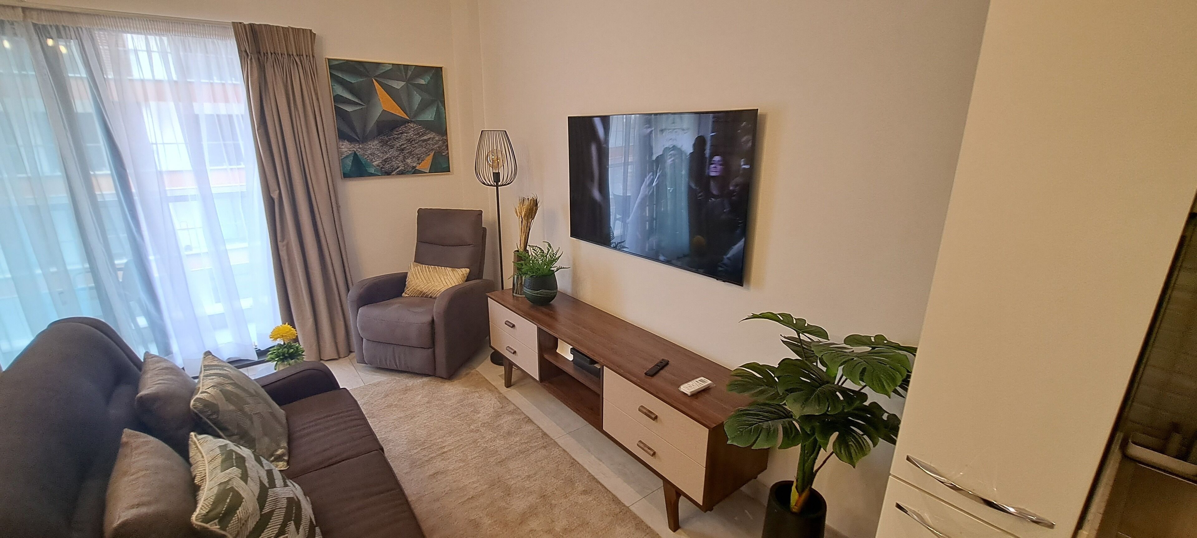 A living room with a sofa, a chair, a wooden side table, a potted plant, and a painting on the wall.