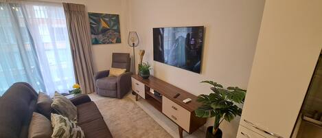 A living room with a sofa, a chair, a wooden side table, a potted plant, and a painting on the wall.