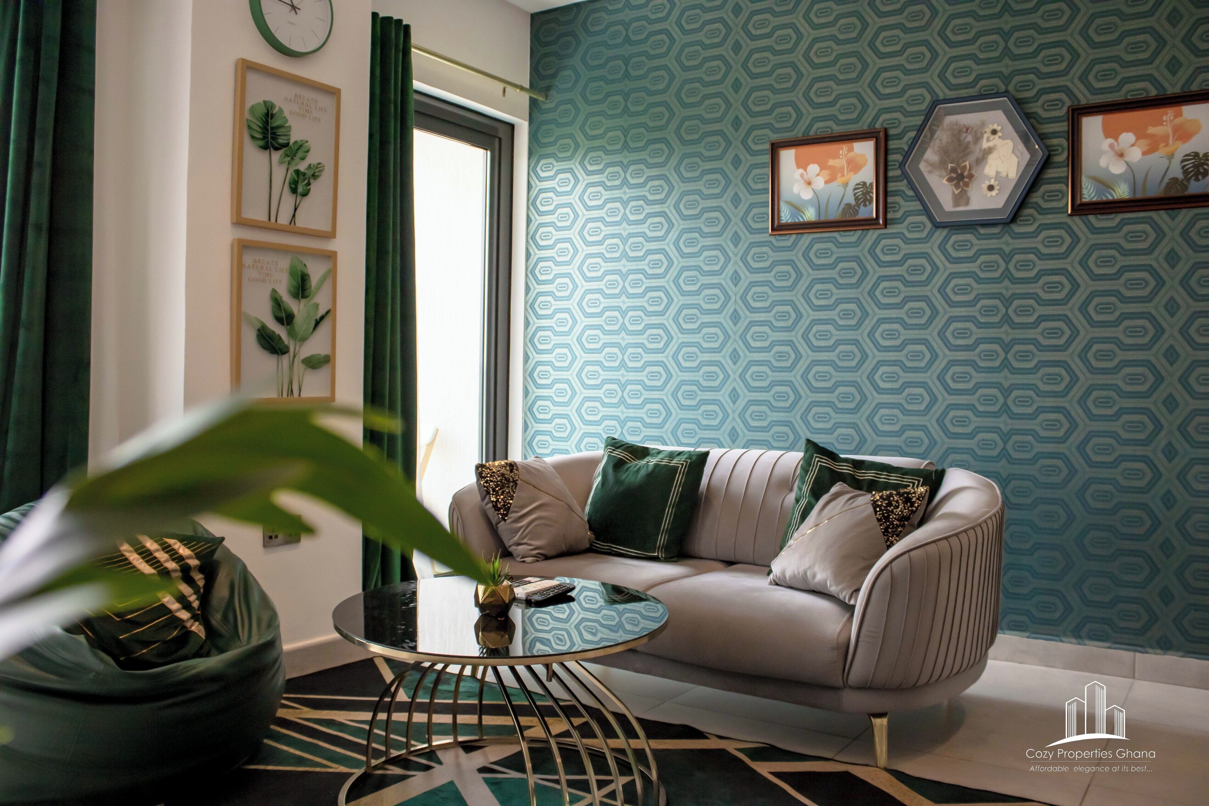 Un salon moderne avec un canapé, une table basse et un fauteuil poire. Des tableaux encadrés ornent le mur, et une fenêtre est agrémentée de rideaux.