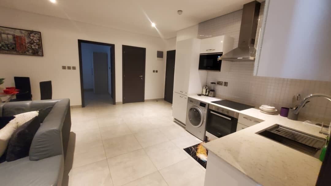 A modern kitchen with a washing machine, a microwave, and a sink. There is a sofa with cushions in the living area.