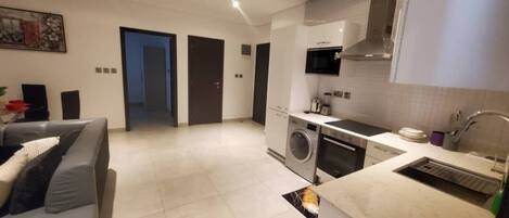 A modern kitchen with a washing machine, a microwave, and a sink. There is a sofa with cushions in the living area.