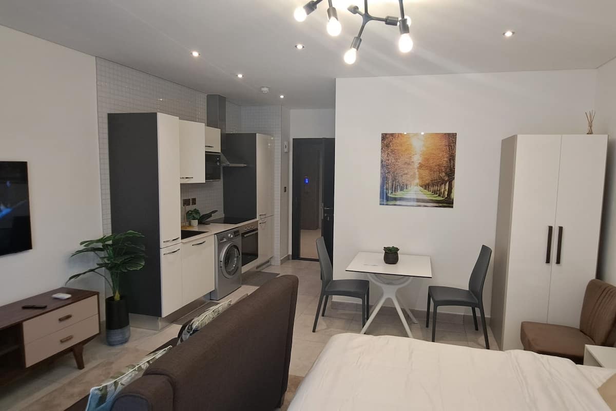 Habitación de hotel moderna con cama, televisión, kitchenette, zona de comedor y baño.