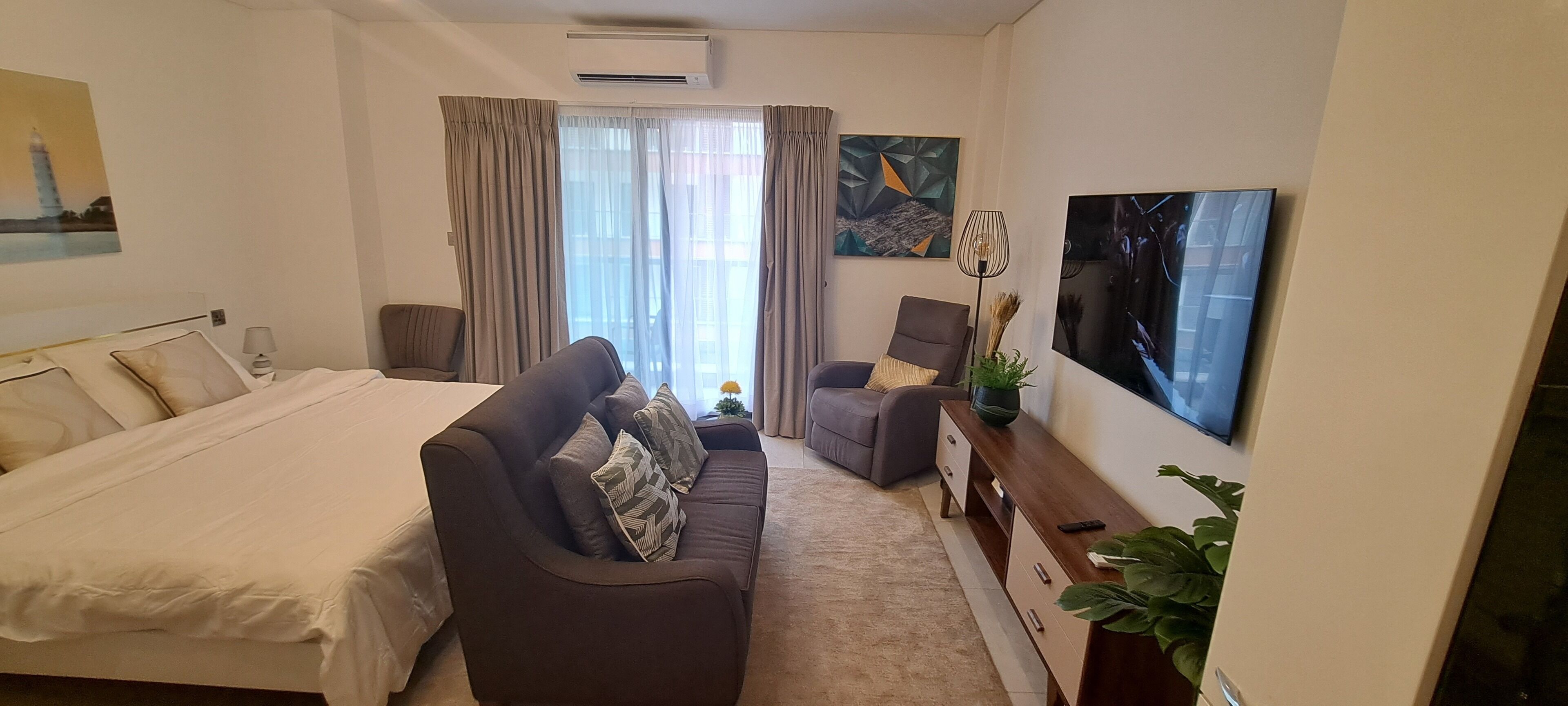 A hotel room with a bed, a sofa, a chair, a TV, and a painting on the wall.
