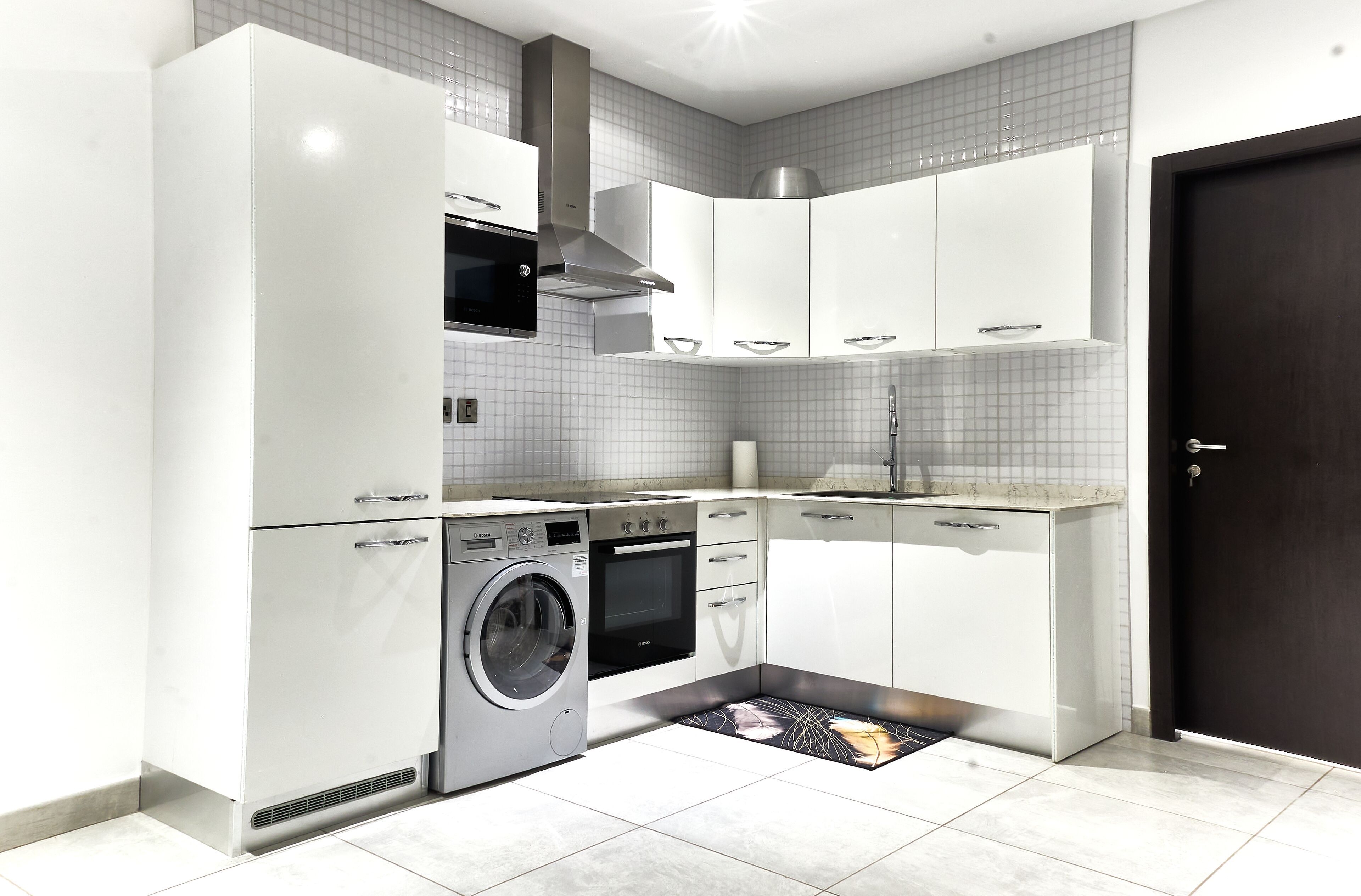 A modern kitchen with white cabinetry, a built-in oven, a microwave, and a washing machine.