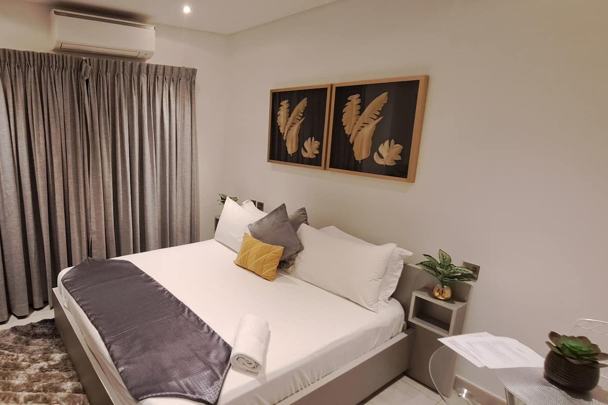 Un dormitorio con cama, cortinas, decoración en la pared, una planta y un escritorio con computadora.