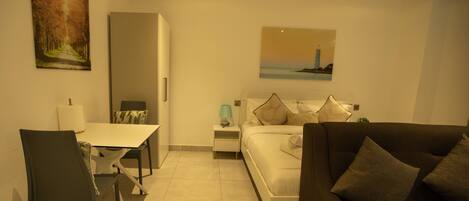 A hotel room with a bed, a sofa, a dining table, and a chair.