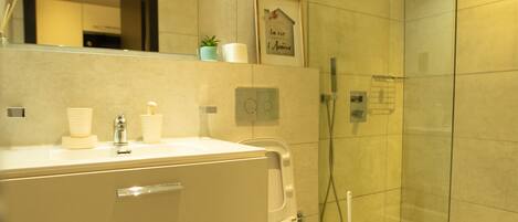 Un baño moderno con cabina de ducha de vidrio, un lavabo blanco con espejo y una pequeña planta en maceta sobre la encimera.