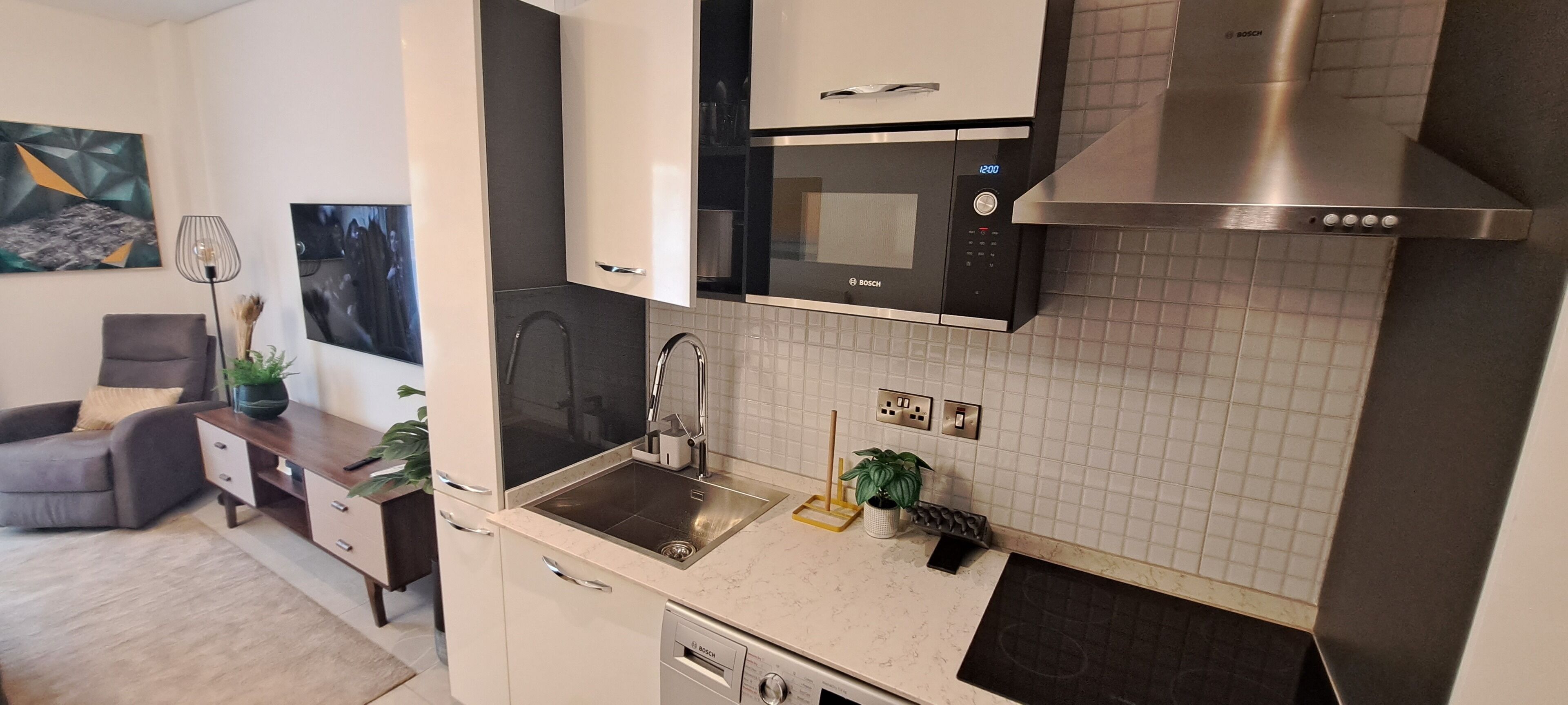 A compact kitchen with a Bosch microwave, a sink, and a dishwasher. There is a small dining area with a sofa and a table.