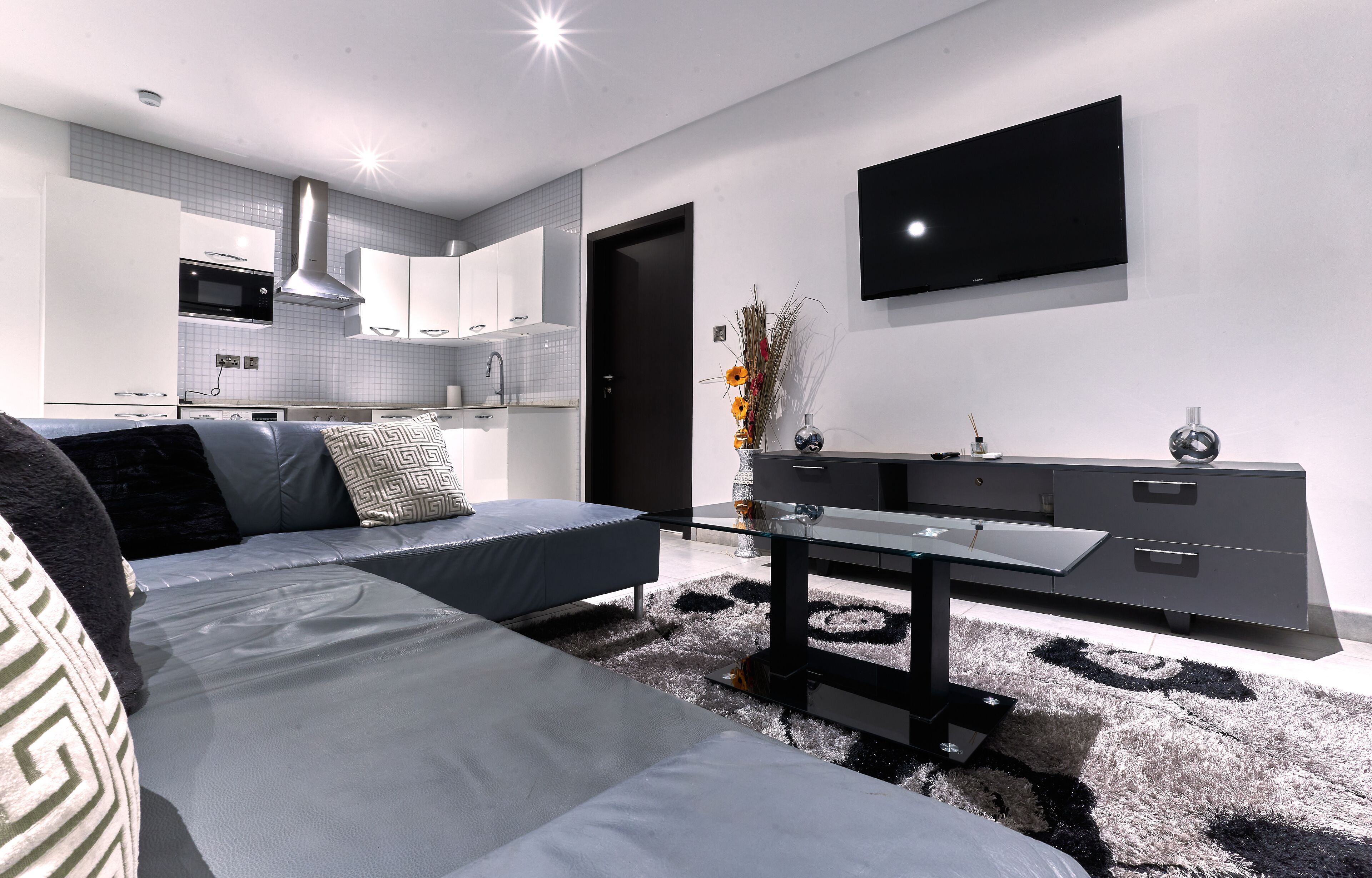 A modern living room with a sofa, a glass coffee table, and a TV mounted on the wall.
