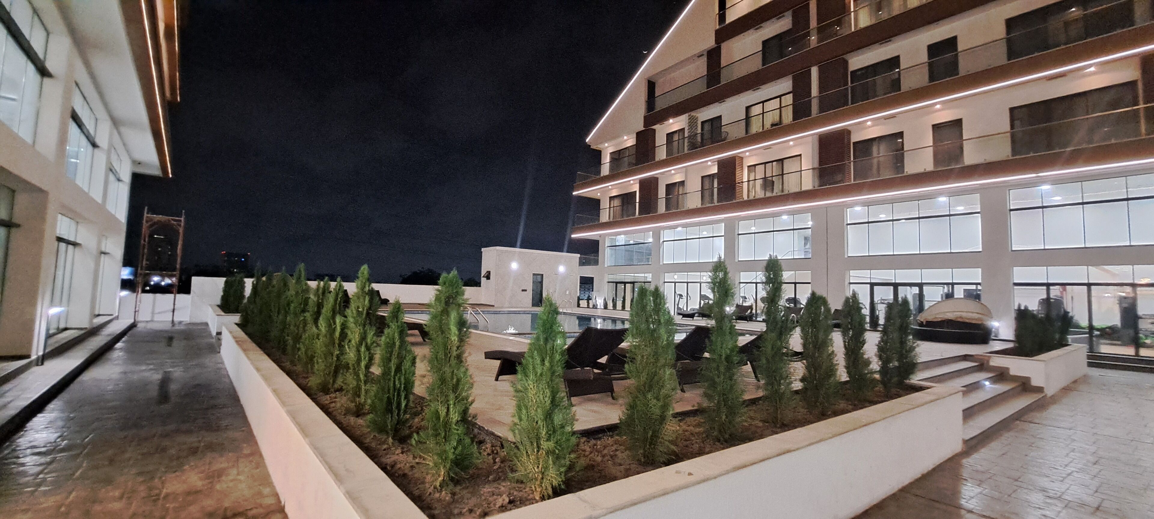 Un edificio moderno con fachada bien iluminada, zona de estar al aire libre y vegetación cuidada.
