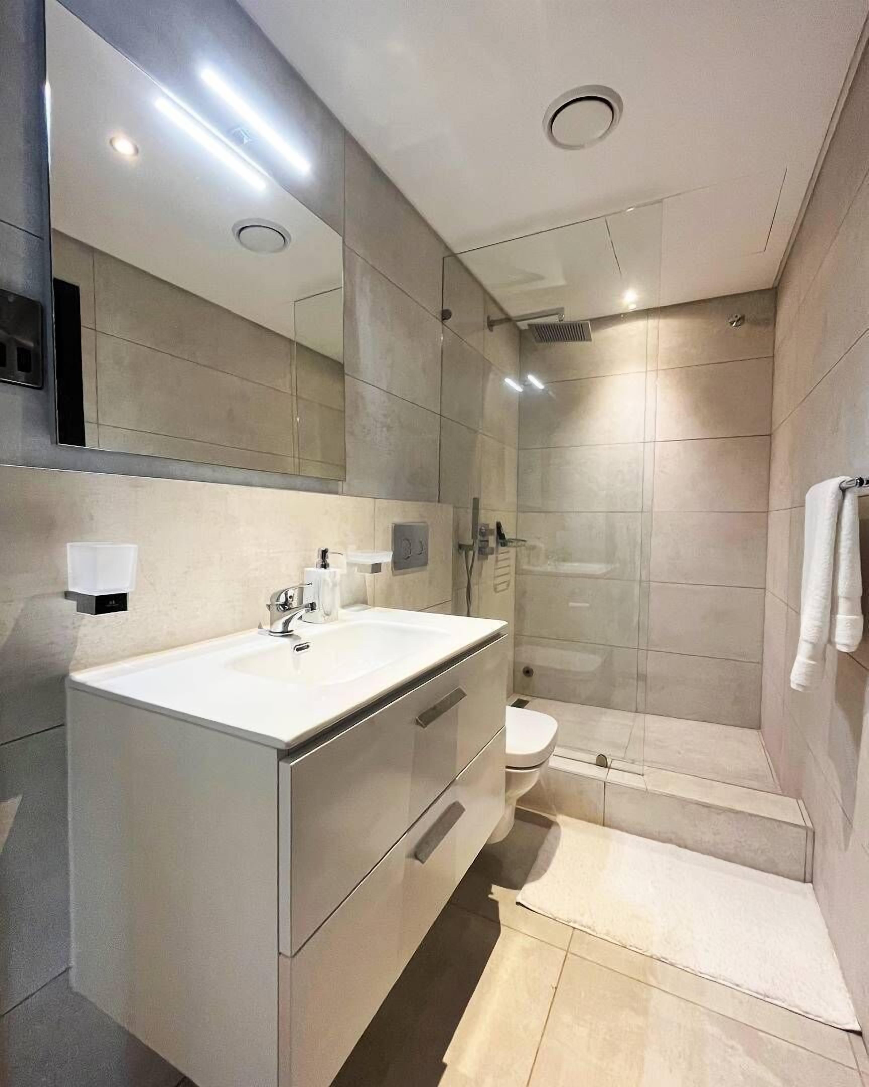A modern bathroom with a large mirror, a sink, a toilet, and a shower area.