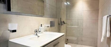 A modern bathroom with a large mirror, a sink, a toilet, and a shower area.