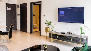 Un salon moderne doté d’un téléviseur à écran plat, d’un coin repas avec une table ronde et des chaises, et d’un couloir menant à une salle de bain.
