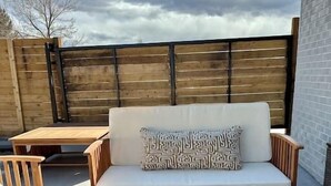 Ein möblierter Patio-Bereich mit gepolsterten Sitzmöglichkeiten, einem kleinen Tisch und einer quadratischen Feuerstelle.