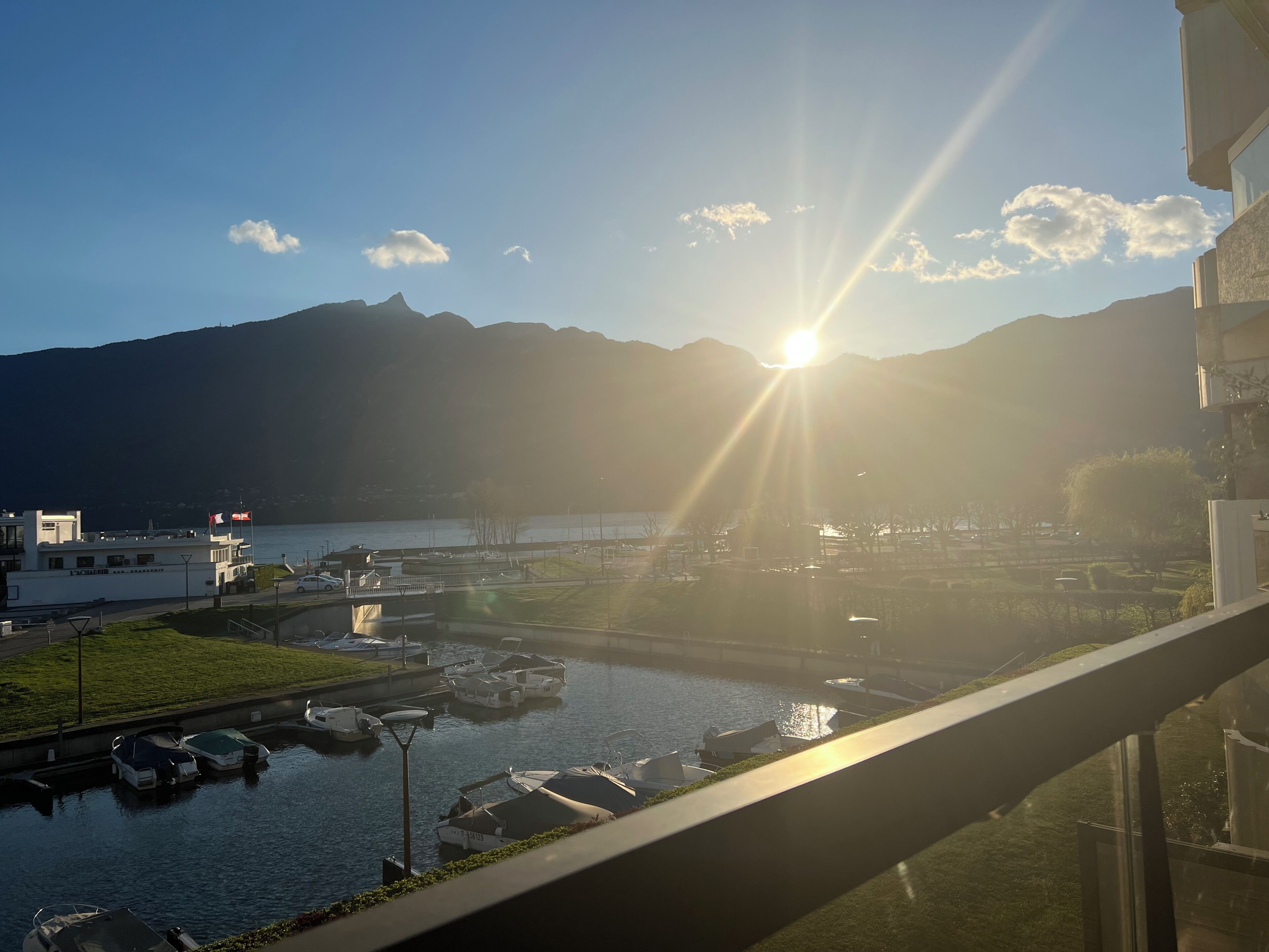 Blick auf eine Marina mit vertäuten Booten, einer Brücke und Bergen im Hintergrund.