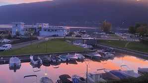 A marina with boats docked, a building complex, and mountains in the background.