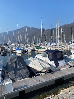 A marina with multiple boats docked, a wooden dock, and mountains in the background.