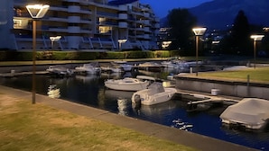 A marina with boats docked, a building with balconies, and a mountain in the background.
