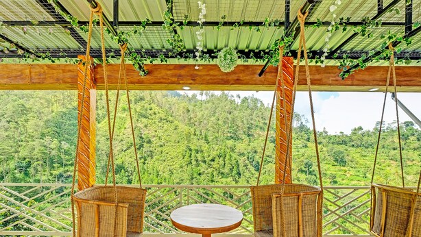Una terraza de madera con una mesa redonda y dos columpios de mimbre con vistas a un bosque frondoso y verde.