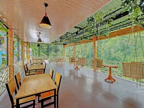 A spacious room with wooden furniture, hanging plants, and large windows offering a view of a forested landscape. - Homes Desa Wisata Conto (Bulukerto)