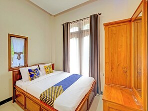 A bedroom with a wooden bed, a window with curtains, and a wooden wardrobe. - Homes Desa Wisata Conto (Bulukerto)