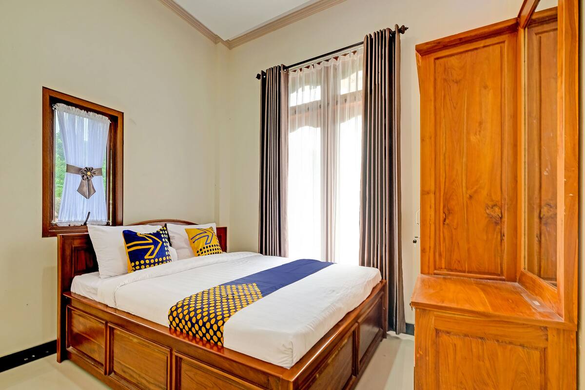A bedroom with a wooden bed, a wardrobe, and a window with curtains.