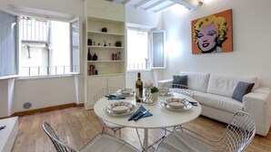 A dining area with a round table, white chairs, and a white sofa. There is a bookshelf with various items and a painting on the wall. - Central Duomo Apartment With Fast Wifi (Florence)