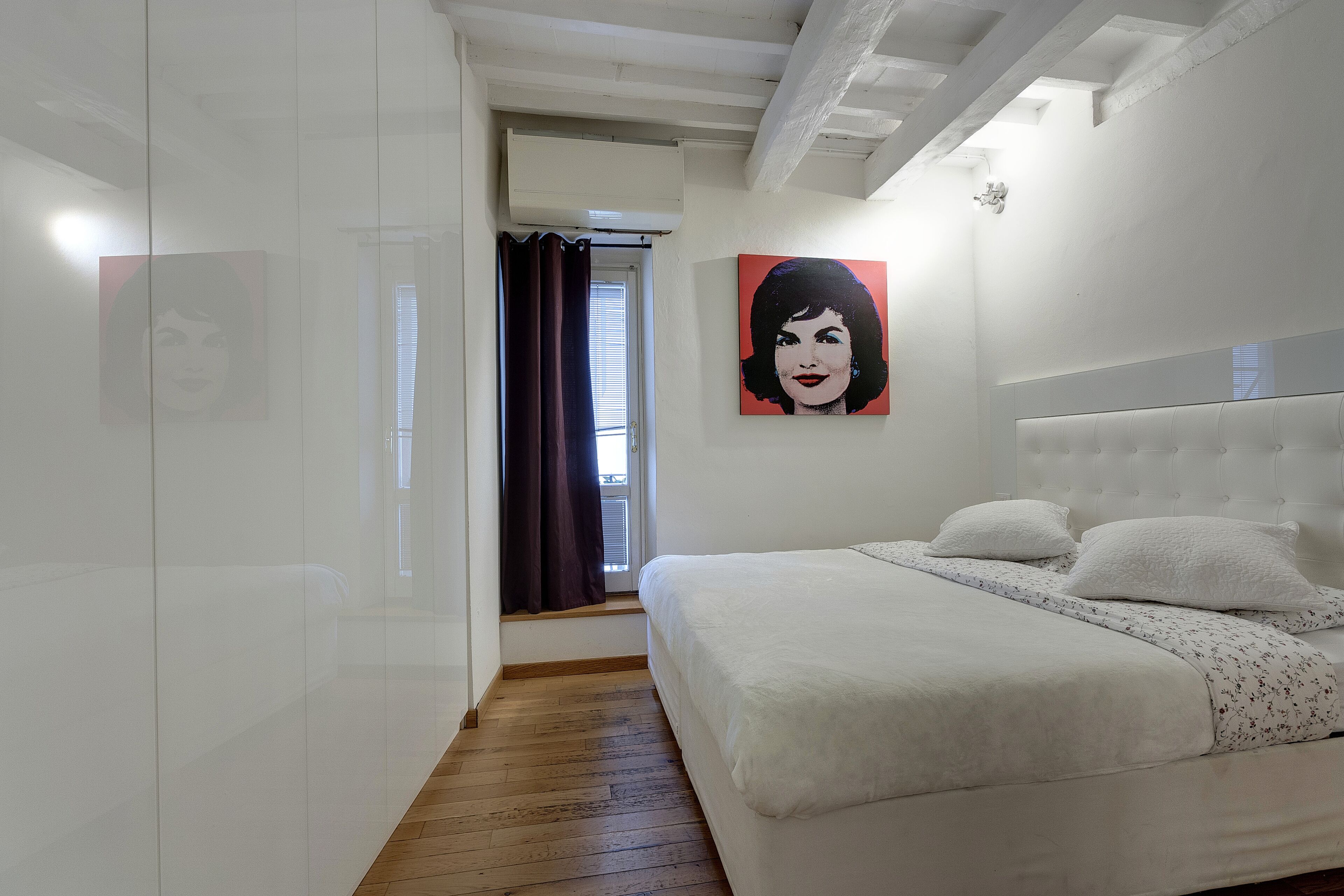 A bedroom with a large bed, a white headboard, and a painting on the wall.