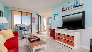 Ein Wohnzimmer mit einem roten Sofa, einem Holztisch, einem Fernseher auf einer weißen Kommode und einer Segelschiff-Dekoration an der Wand.