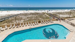 Ein Pool mit Delphin-Motiv, umgeben von Liegestühlen und Blick auf den Strand.